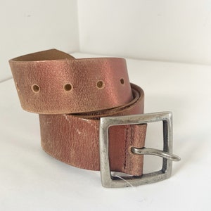May include: A brown leather belt with a silver buckle. The belt has a distressed look and is rolled up.