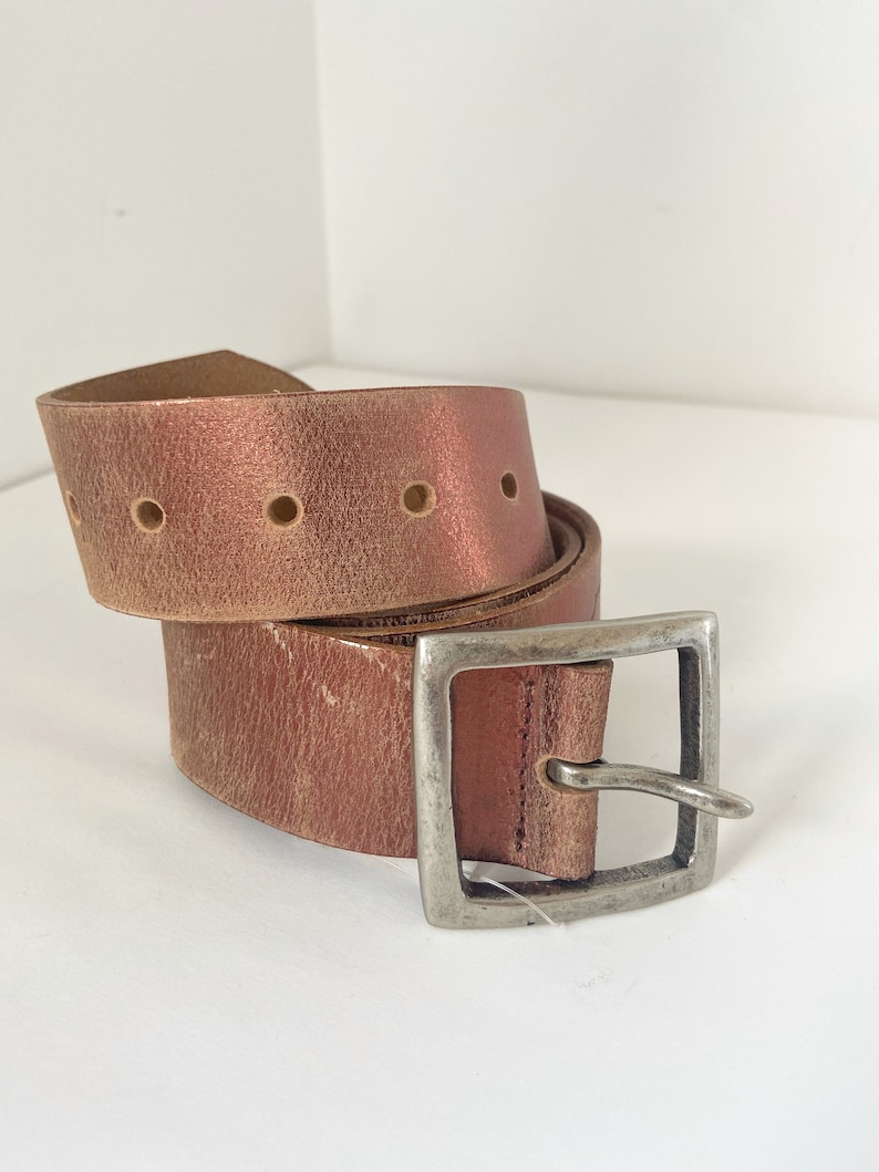 May include: A brown leather belt with a silver buckle. The belt has a distressed look and is rolled up.