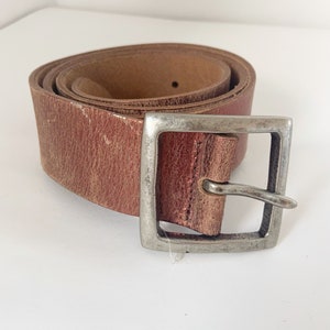 May include: A brown leather belt with a silver buckle. The belt is rolled up and the buckle is on the right side of the image.
