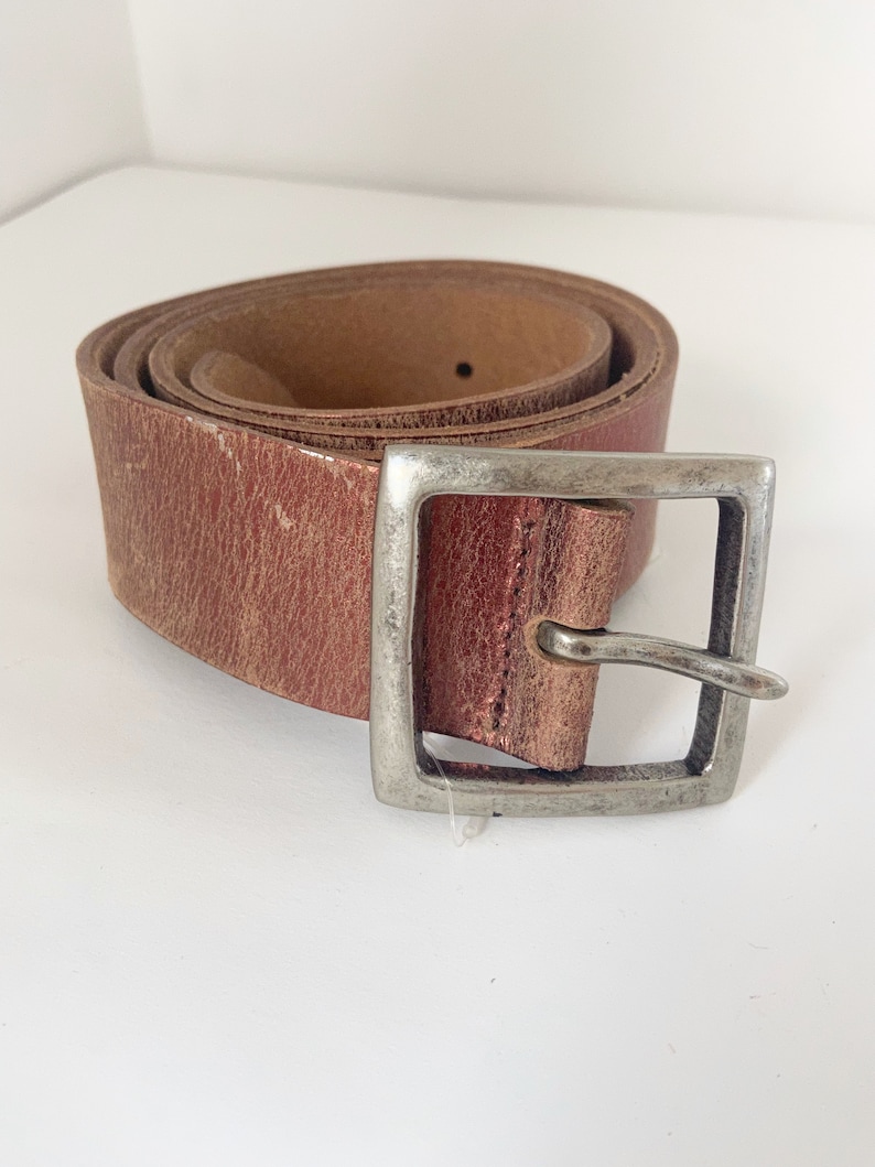 May include: A brown leather belt with a silver buckle. The belt is rolled up and the buckle is on the right side of the image.