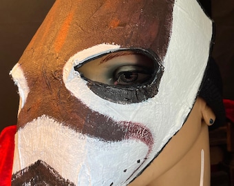 May include: A handmade badger mask with a brown and white painted design. The mask features a black nose and ears, with white whiskers attached. The mask is worn by a mannequin.
