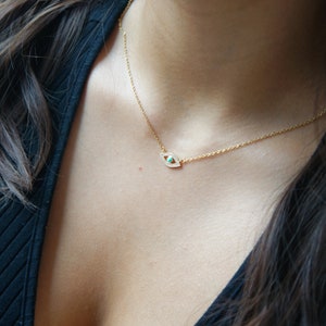 May include: A gold chain necklace with a small evil eye pendant. The pendant is set with tiny clear stones and a turquoise blue stone in the center.