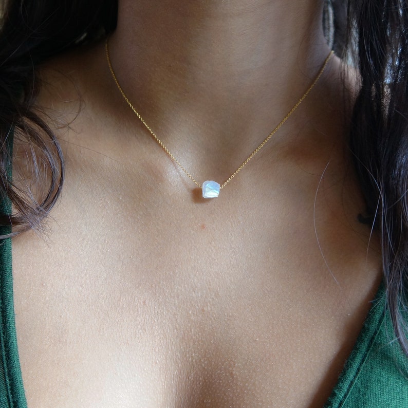 May include: A gold chain necklace with a single iridescent white gemstone pendant.