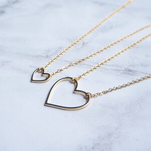 Puede incluir: Tres collares de oro con colgantes de coraz&oacute;n de diferentes tama&ntilde;os. Los collares est&aacute;n superpuestos sobre una superficie de m&aacute;rmol blanco.