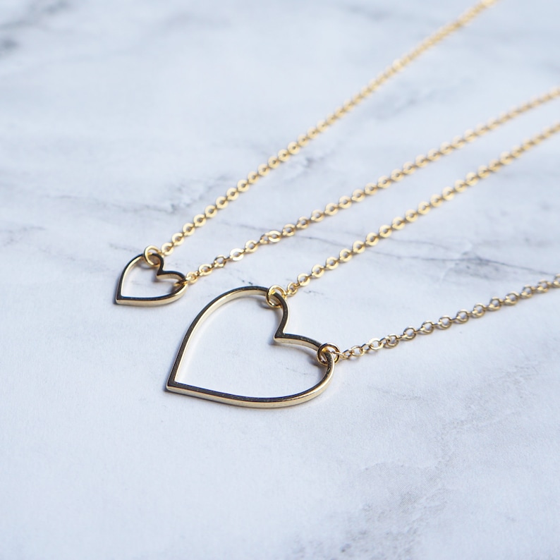 Puede incluir: Tres collares de oro con colgantes de coraz&oacute;n de diferentes tama&ntilde;os. Los collares est&aacute;n superpuestos sobre una superficie de m&aacute;rmol blanco.