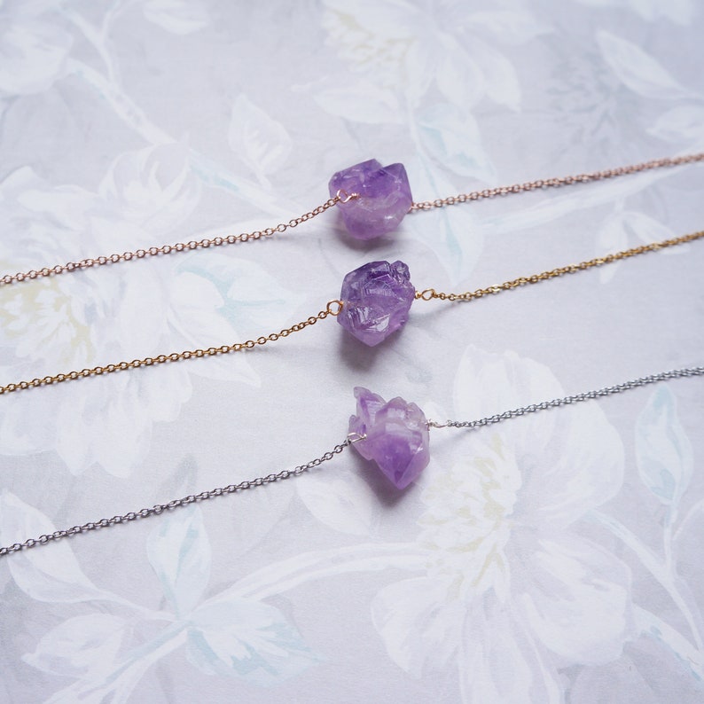 Puede incluir: Tres delicados collares con colgantes de cristal de amatista. Cada collar presenta un estilo de cadena diferente: oro rosa, oro y plata.