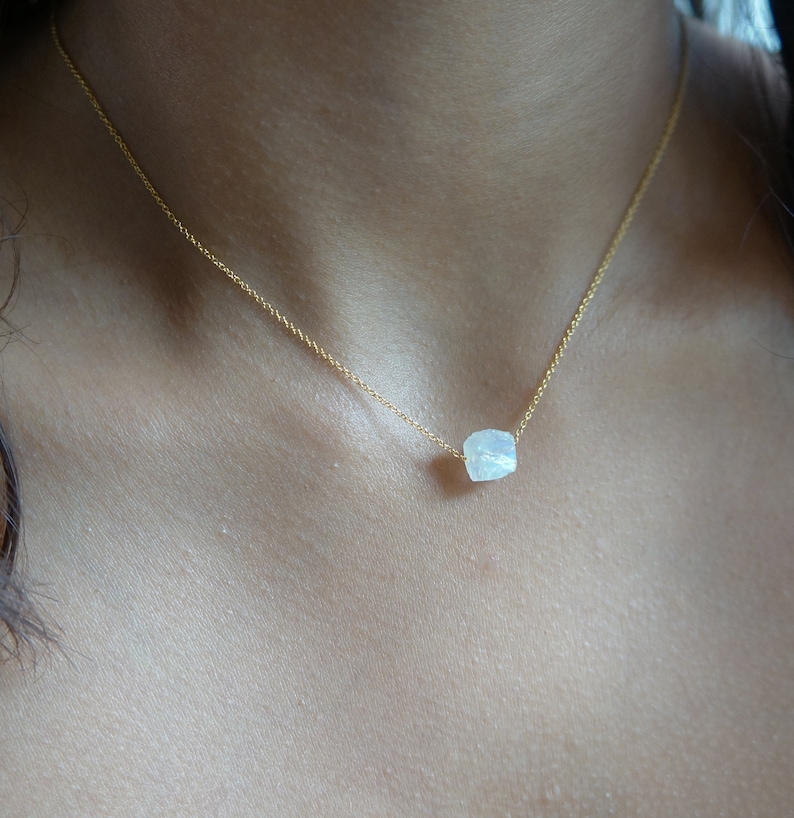 May include: A delicate gold chain necklace with a single, white, faceted gemstone pendant.