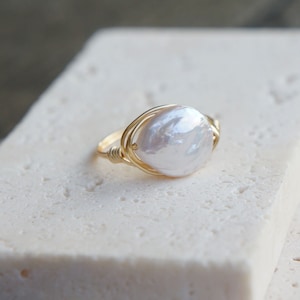May include: A gold wire wrapped ring with a large white baroque pearl.