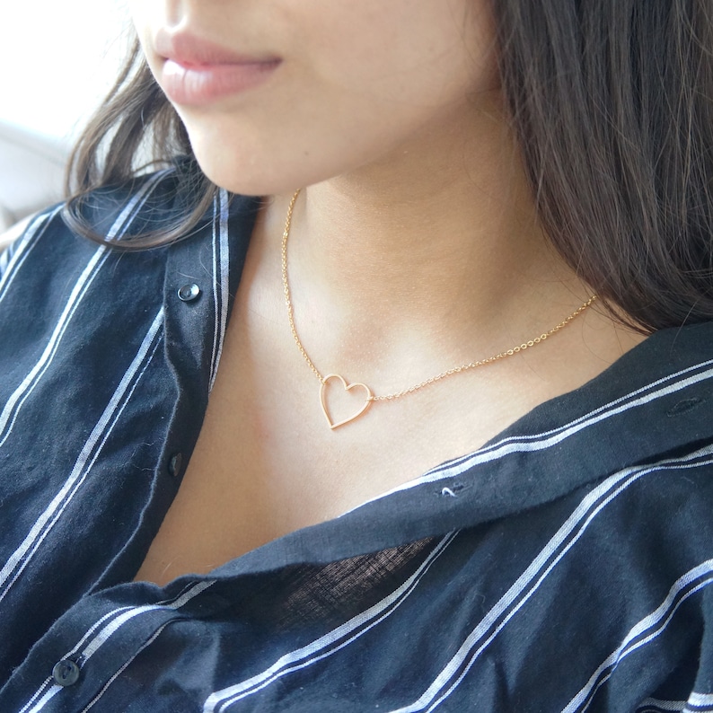 Puede incluir: Un collar de cadena dorada con un delicado colgante de coraz&oacute;n abierto.