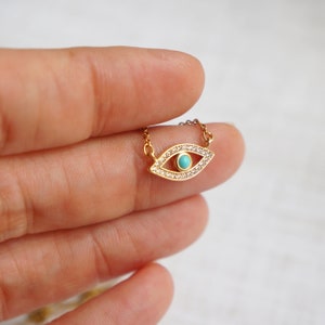 May include: A gold necklace with a turquoise evil eye charm surrounded by clear cubic zirconia stones.