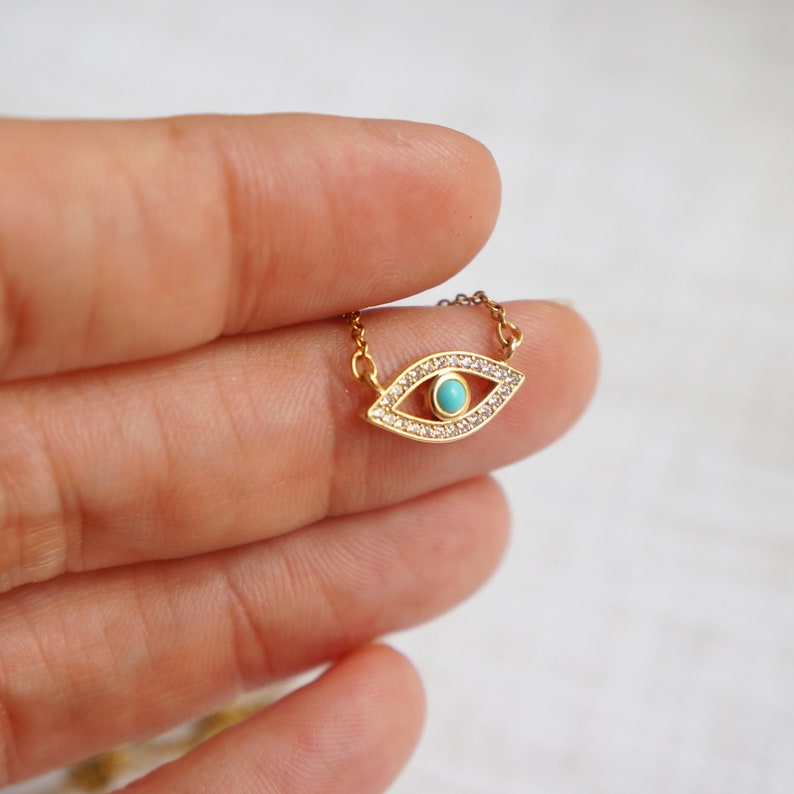 May include: A gold necklace with a turquoise evil eye charm surrounded by clear cubic zirconia stones.