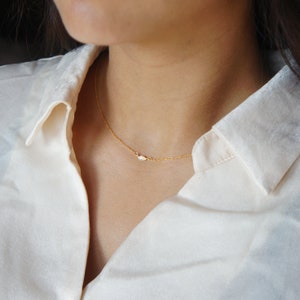 May include: A delicate gold chain necklace with a small, oval-shaped pendant. The pendant has a subtle sparkle.