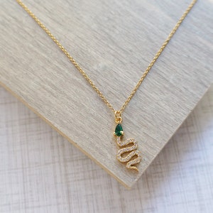May include: A gold chain necklace with a snake pendant. The snake is encrusted with clear rhinestones and has a green gemstone for a head.