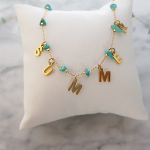 May include: A gold chain necklace with turquoise beads and gold letter charms spelling out the word "SUMMER".