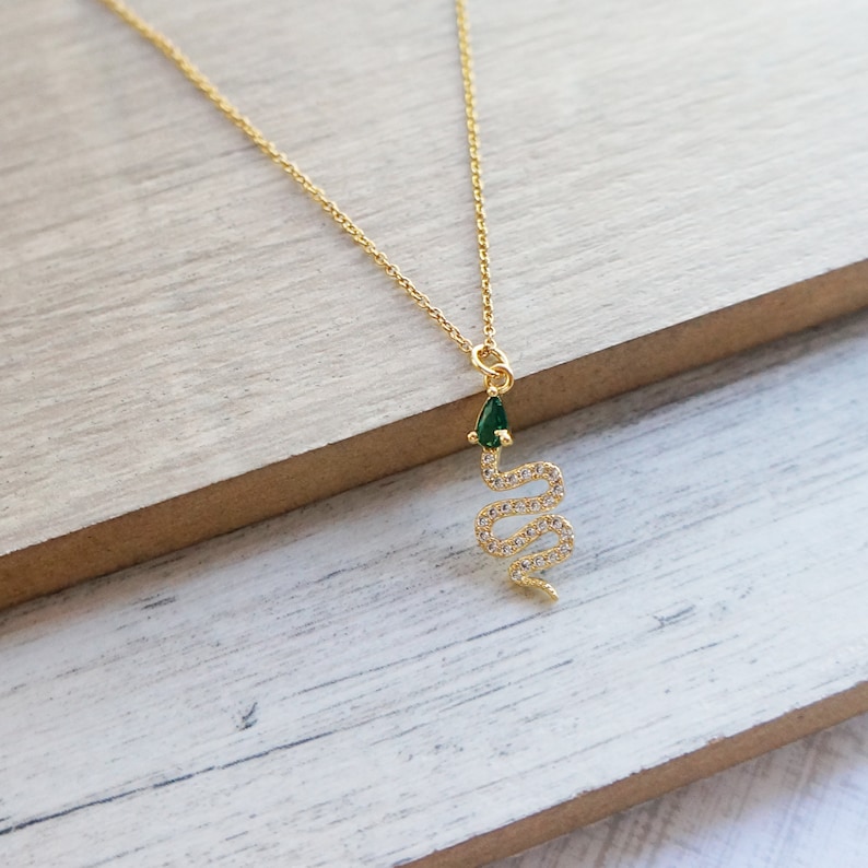 May include: A gold snake necklace with a green gemstone on the head. The snake is encrusted with clear rhinestones.