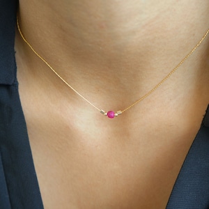 May include: A delicate gold chain necklace with a single pink gemstone bead and two small gold beads.