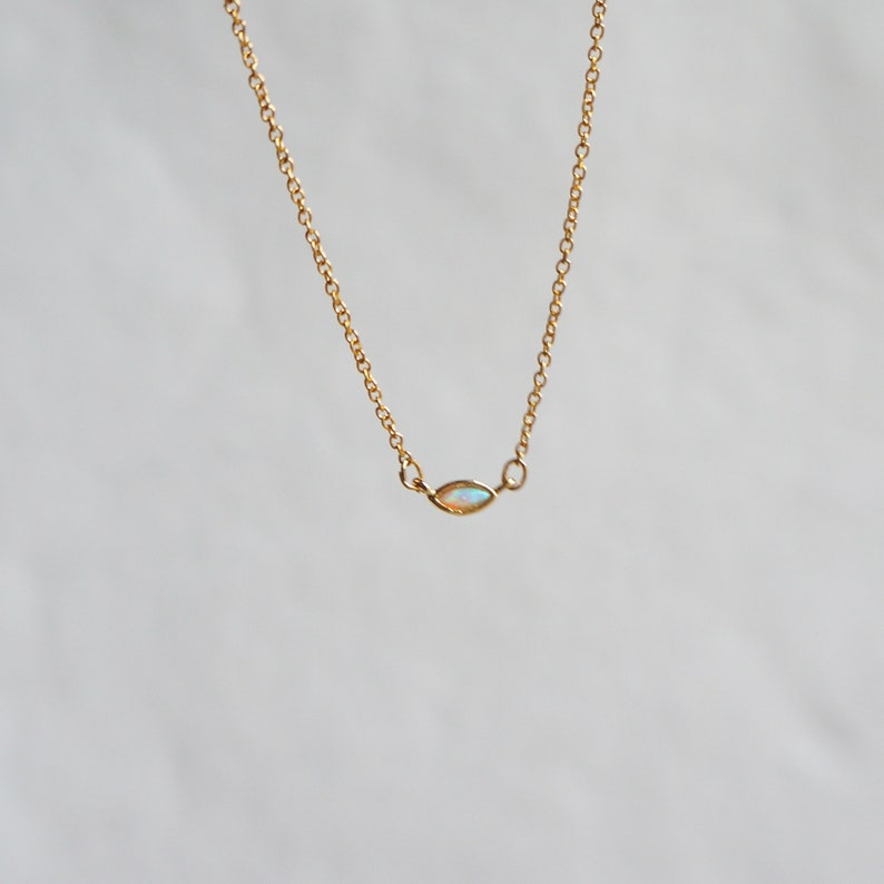 May include: A delicate gold chain necklace with a small, oval-shaped opal pendant.