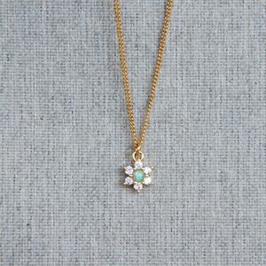 May include: A gold chain necklace with a small flower pendant. The flower has a light blue centre and is surrounded by clear rhinestones.