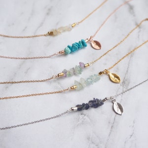 May include: Five delicate gold necklaces with small, natural stone charms and a gold leaf pendant. Each necklace features a different type of stone, including turquoise, amethyst, and aquamarine.