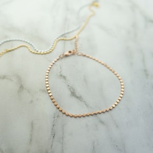 Puede incluir: Un delicado brazalete de cadena de oro rosa con un dise&ntilde;o de eslabones peque&ntilde;os y redondos. El brazalete est&aacute; hecho de metal y tiene un estilo simple y elegante.