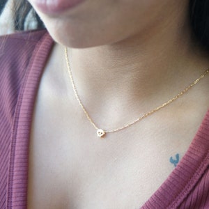 May include: A gold chain necklace with a small skull pendant. The necklace is worn by a person with a red shirt.