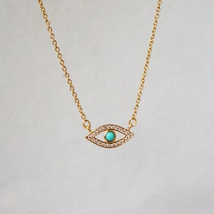 May include: A gold chain necklace with a turquoise and clear crystal evil eye pendant.