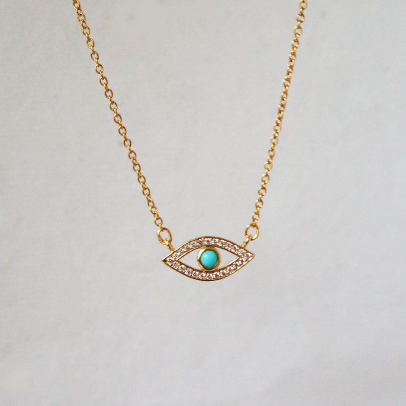 May include: A gold chain necklace with a turquoise and clear crystal evil eye pendant.