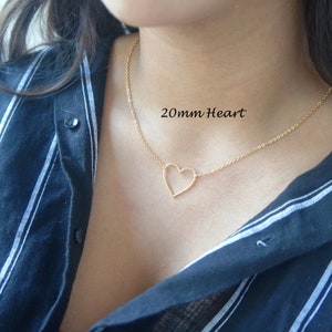 Puede incluir: Un collar de cadena dorada con un colgante de coraz&oacute;n abierto de 20 mm. El collar lo lleva una persona con una camisa de rayas blancas y negras.