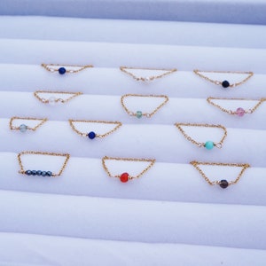 May include: A set of 10 delicate gold chain rings, each featuring a different colored gemstone bead. The beads are arranged in a row on a white surface.