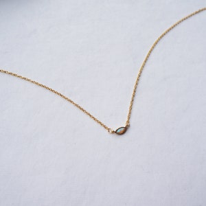 May include: A delicate gold chain necklace with a small, iridescent opal pendant in the shape of a marquise.