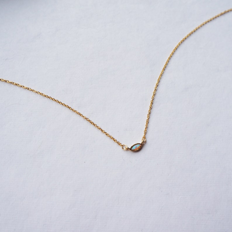 May include: A delicate gold chain necklace with a small, iridescent opal pendant in the shape of a marquise.