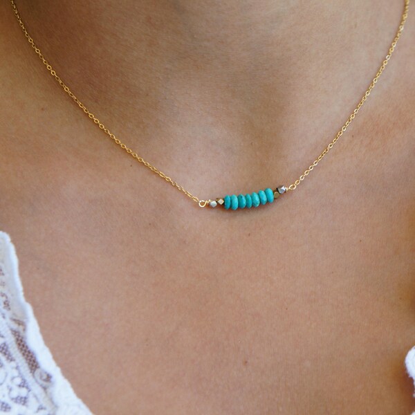 Op de afbeelding: Een delicate gouden ketting met een rij kleine, levendige turquoise kralen. De kralen zijn geregen met kleine zilverkleurige kralen. De ketting heeft een dunne, gouden ketting en wordt gepresenteerd tegen een neutrale achtergrond.