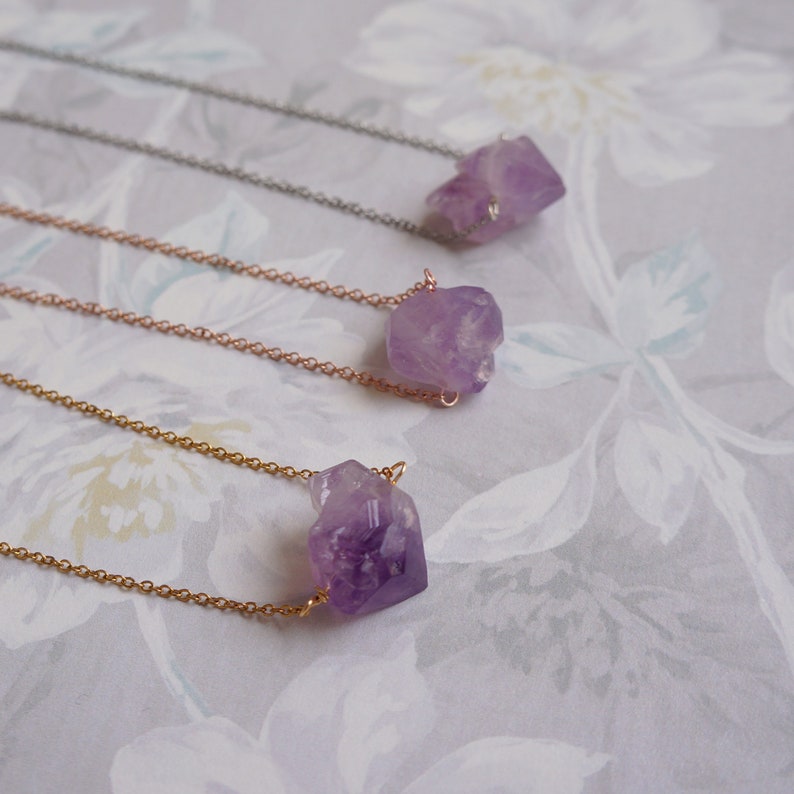 Puede incluir: Tres delicados collares con colgantes de cristal de amatista. Cada collar presenta un estilo de cadena diferente: plata, oro rosa y oro.