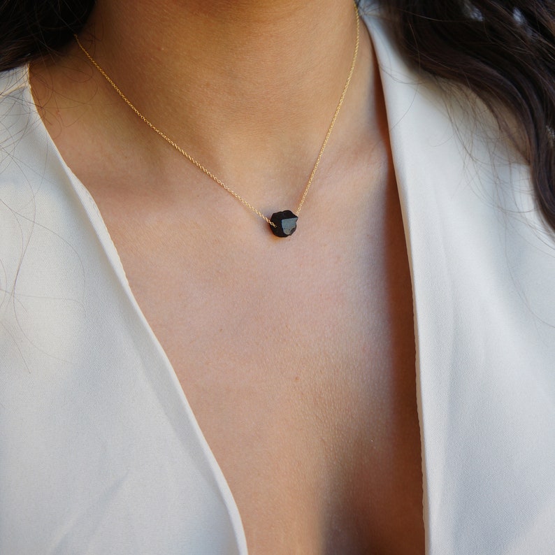 Puede incluir: Un delicado collar de cadena dorada con un solo colgante de piedra negra facetada.