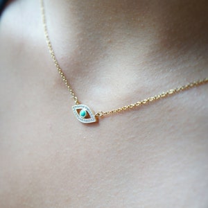 May include: A gold chain necklace with a turquoise and clear crystal evil eye pendant.