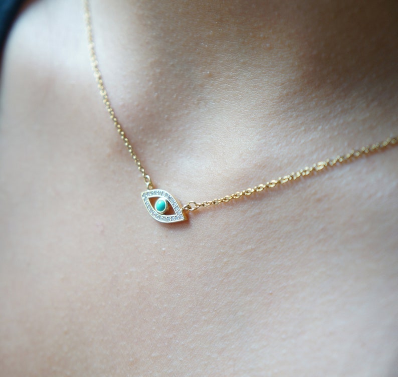 May include: A gold chain necklace with a turquoise and clear crystal evil eye pendant.