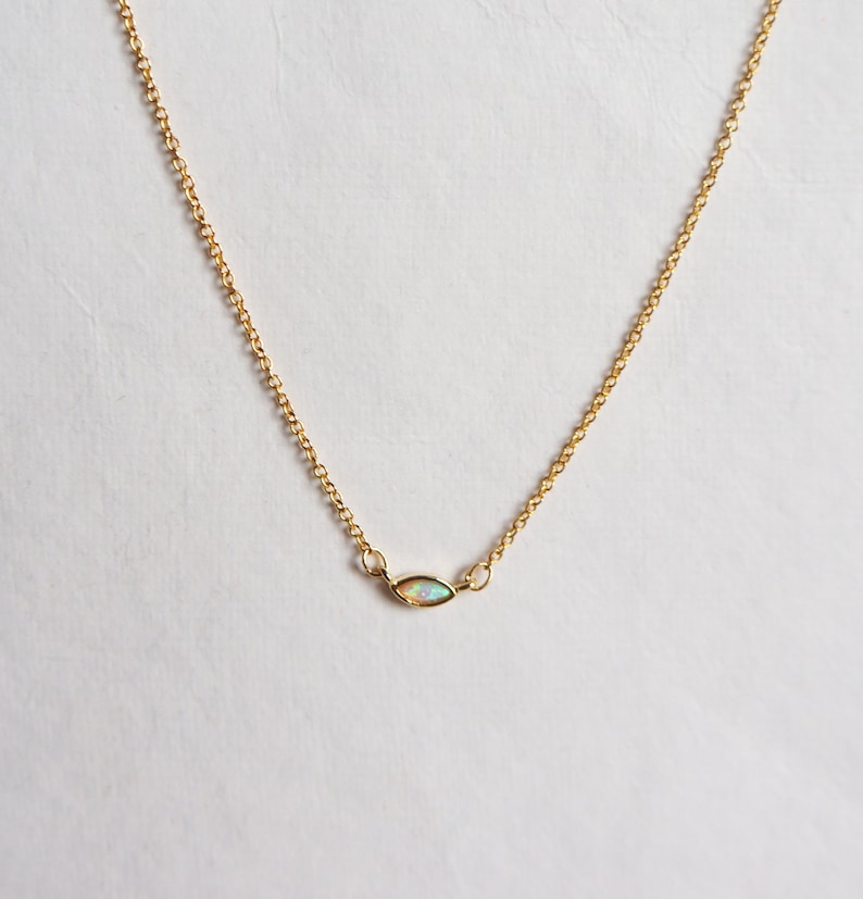 May include: A delicate gold chain necklace with a small, oval-shaped opal pendant.
