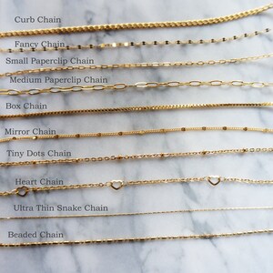May include: A collection of gold-colored chain necklaces, each with a unique design. Styles include curb, fancy, paperclip, box, mirror, tiny dots, heart, ultra-thin snake, and beaded chains. The names of each chain style are displayed above each chain.