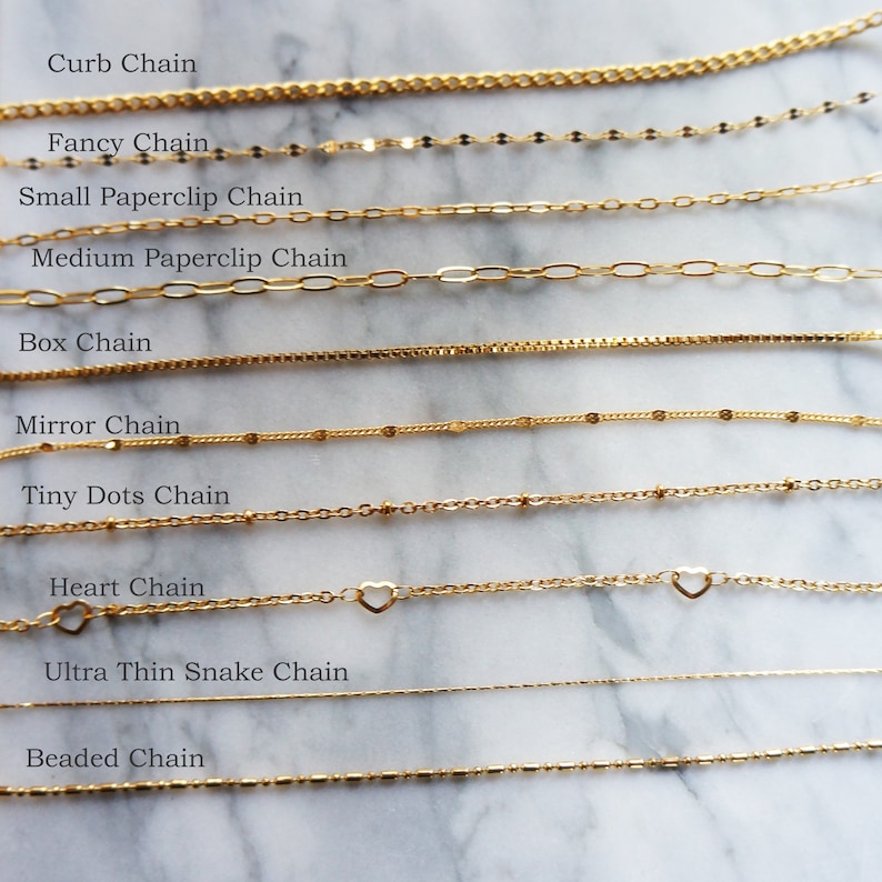 May include: A collection of gold-colored chain necklaces, each with a unique design. Styles include curb, fancy, paperclip, box, mirror, tiny dots, heart, ultra-thin snake, and beaded chains. The names of each chain style are displayed above each chain.