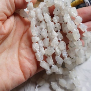 May include: A strand of white moonstone beads, each bead is a rough, irregular shape with a slightly iridescent sheen.
