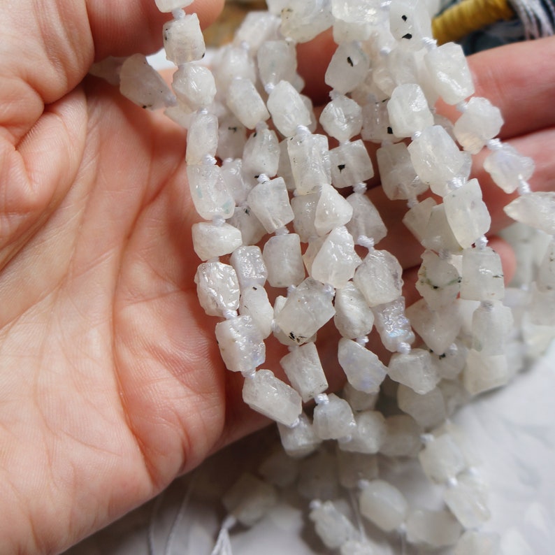 May include: A strand of white moonstone beads, each bead is a rough, irregular shape with a slightly iridescent sheen.