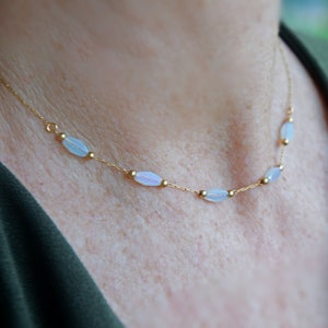 May include: A delicate gold chain necklace with oval-shaped white opal beads.