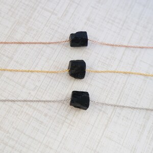 Puede incluir: Tres collares con piedras de turmalina negra en cadenas de diferentes colores. El collar superior tiene una cadena de oro rosa, el collar del medio tiene una cadena de oro y el collar inferior tiene una cadena de plata.