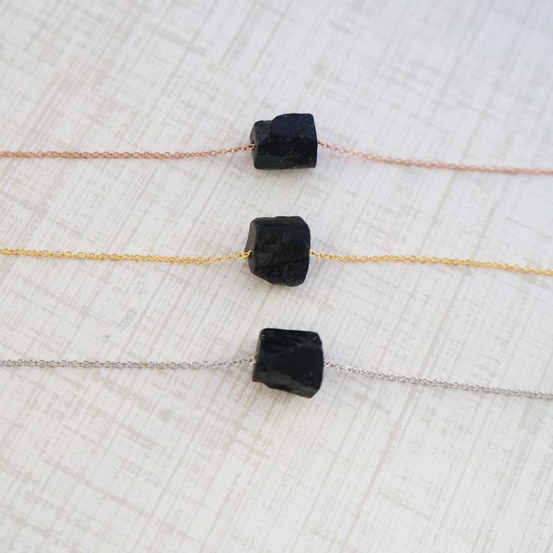 Puede incluir: Tres collares con piedras de turmalina negra en cadenas de diferentes colores. El collar superior tiene una cadena de oro rosa, el collar del medio tiene una cadena de oro y el collar inferior tiene una cadena de plata.