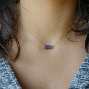 May include: A delicate gold chain necklace with a single, small, rectangular amethyst gemstone pendant.