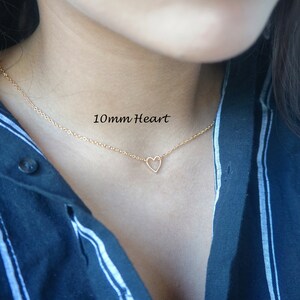 Puede incluir: Un collar de cadena dorada con un colgante de coraz&oacute;n abierto de 10 mm. El collar lo lleva una persona con una camisa a rayas azules y blancas.