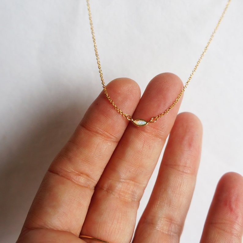 May include: A delicate gold chain necklace with a small, oval-shaped opal pendant.