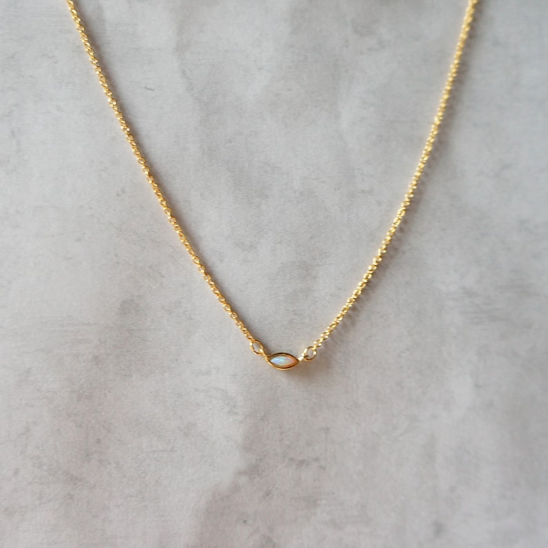 May include: A delicate gold chain necklace with a small, oval-shaped opal pendant.
