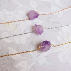 Puede incluir: Tres delicados collares con colgantes de cristal de amatista. Cada collar presenta un estilo de cadena diferente: oro rosa, plata y oro.