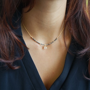 May include: A delicate gold chain necklace with small black beads and a small white pearl pendant.